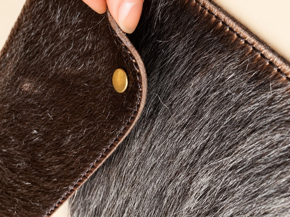 Close-up of cowhide hair texture, stitched edge and round gold-tone fastening