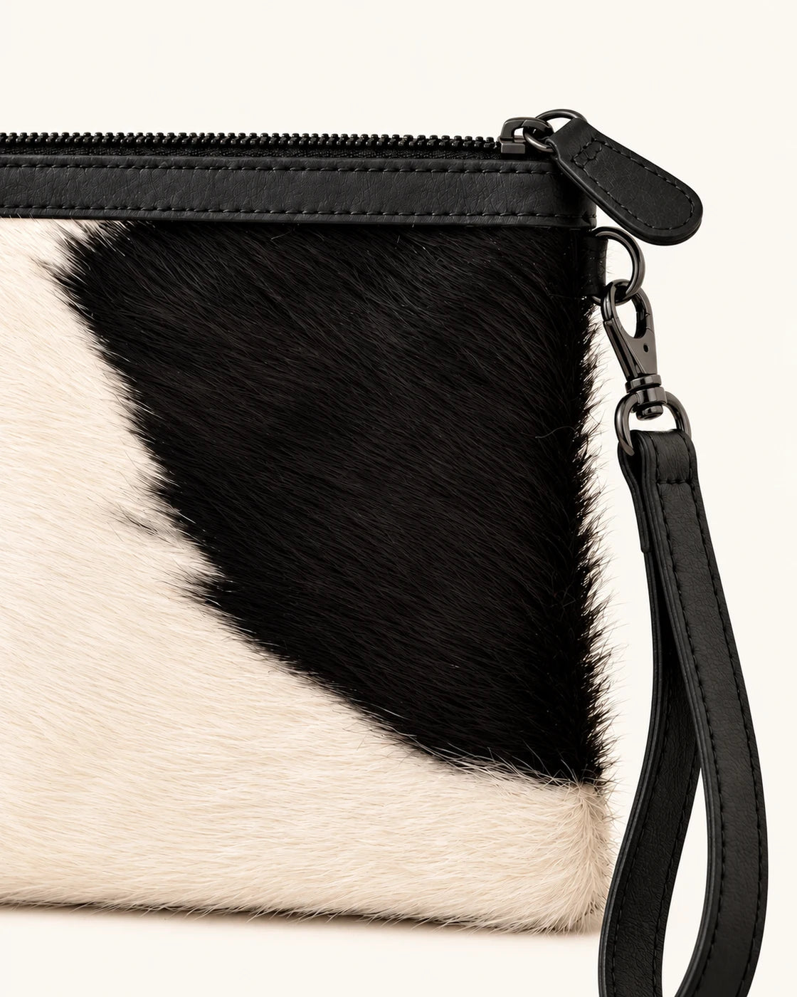 Close-up of cowhide hair texture, black leather zipper trim and wrist-strap hardware; AI-assisted product image.
