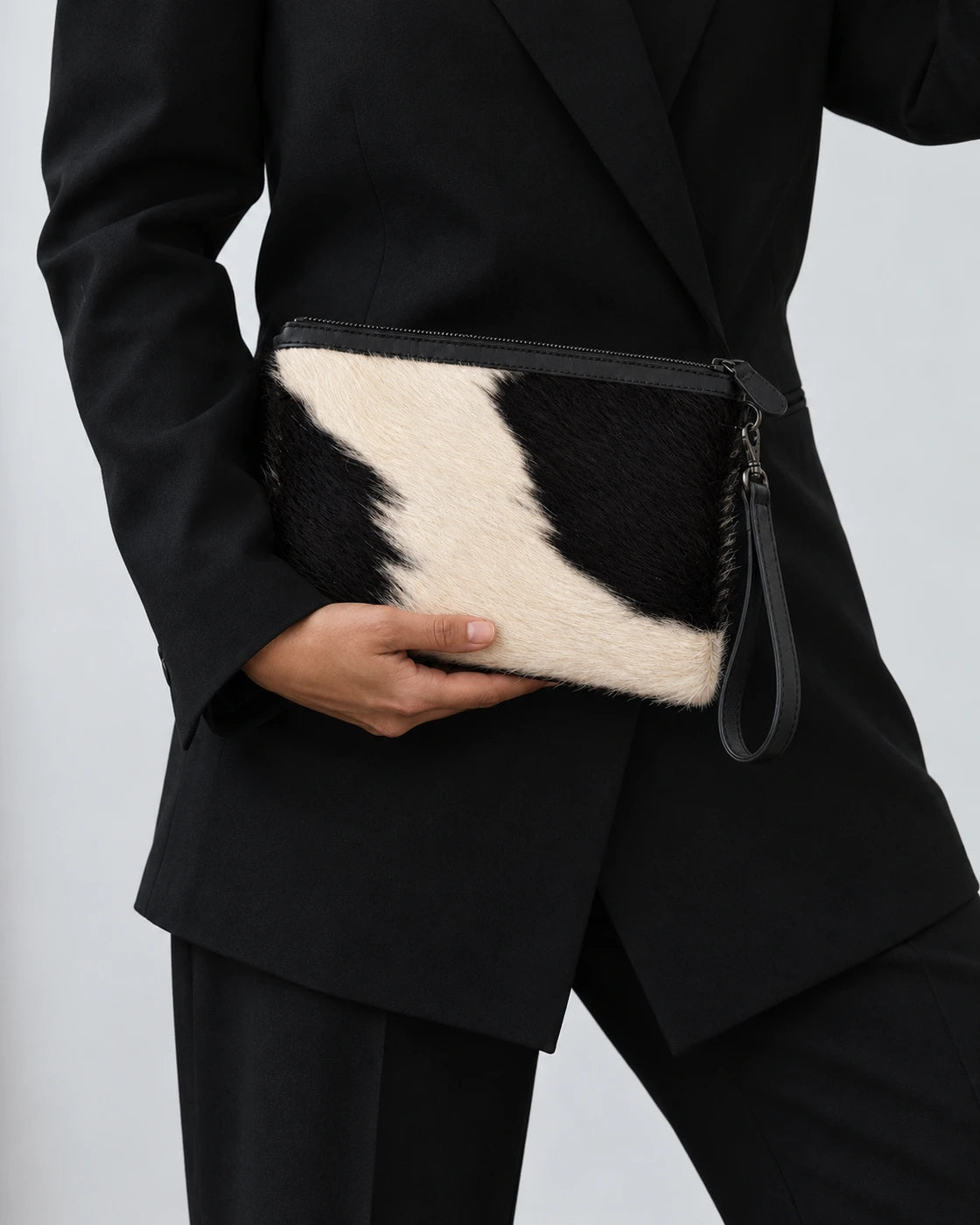 ADEEM clutch held at the waist with a black tailored outfit, face outside frame; AI-generated styling illustration.